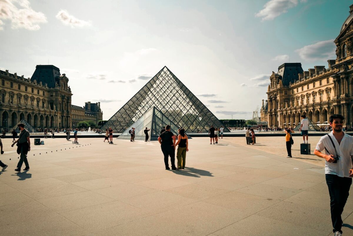 A daytime view of the Louvre Pyramid in Paris with people walking around.