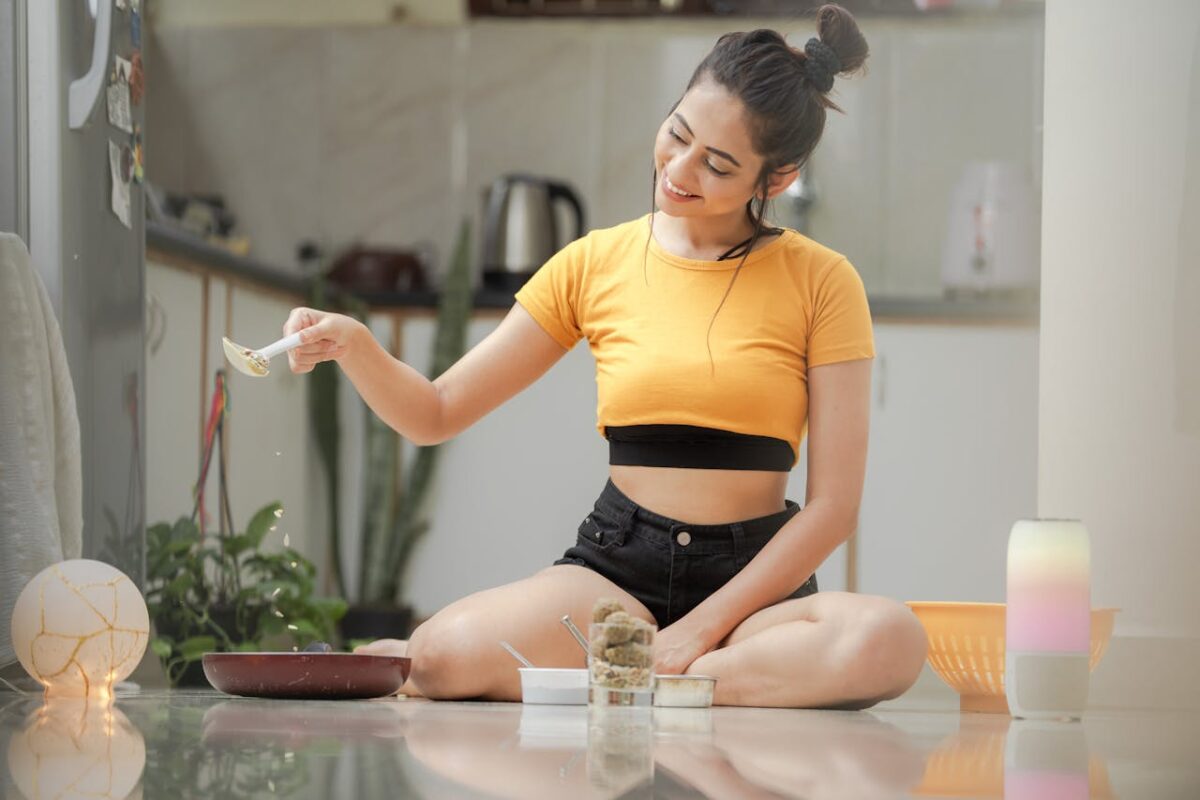 Young woman joyfully cooking in a modern kitchen setting, seated casually on the floor.