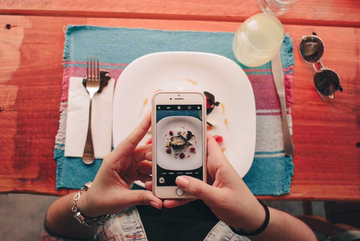 A woman takes a photo of a dessert with her smartphone at a restaurant.
