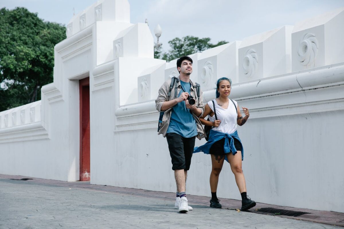 Young tourists exploring a city, walking by a historic white wall on a bright day.